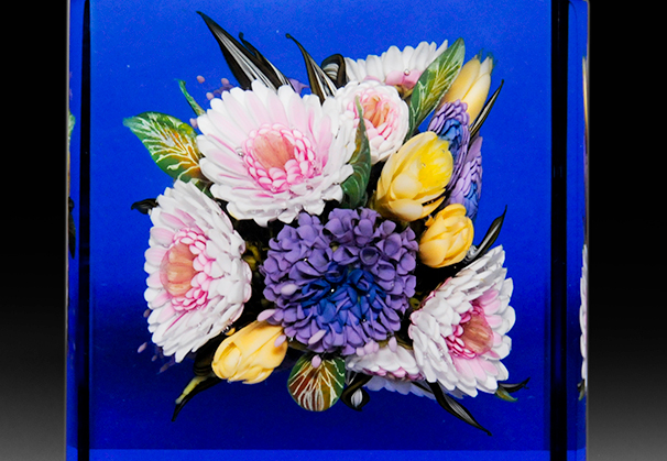 Untitled, 2018; 3-9/16 x 2-3/4 inches; flame-worked chrysanthemum and bachelor’s button bouquet in blue cube paperweight.