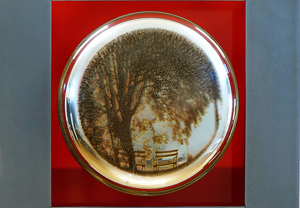 <i>Tree with Bench</i>, 2021; 14 h x 13.5 w 4.25 d (inches); original image, screen-printed kiln-fired enamels, blown, sandblasted, mirrored glass, steel with patina and paint

